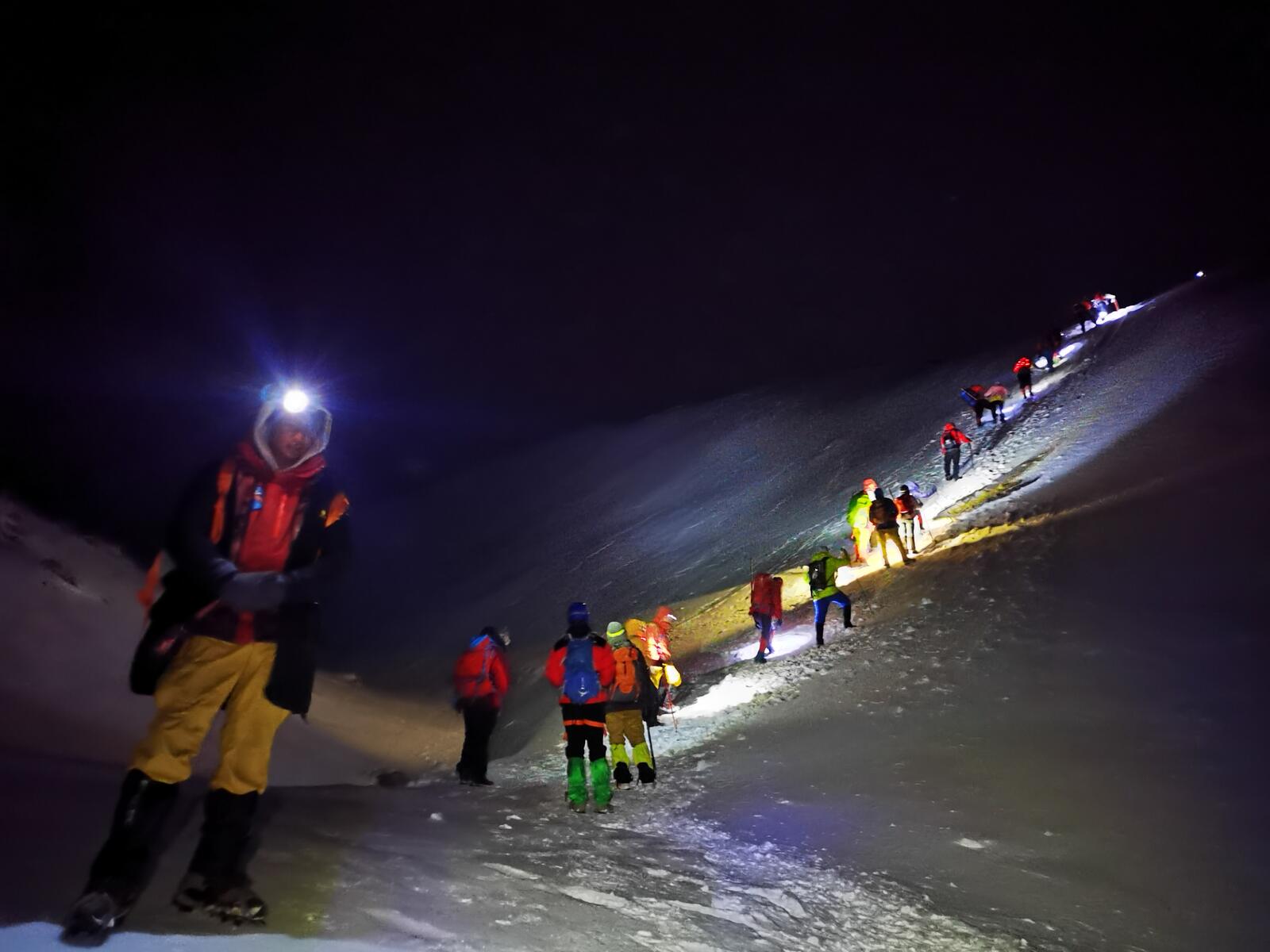 A line of climbers ascending a dark ridge by headlamp.