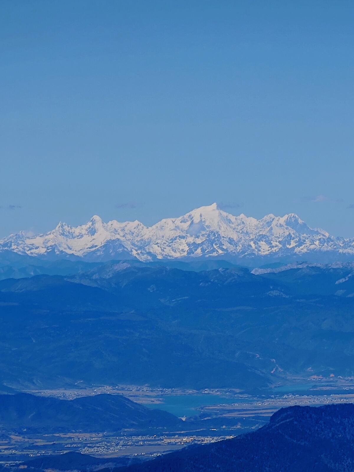 Kawa Karpo, the sacred unclimbed peak, seen from Haba's summit with a turquoise valley below.