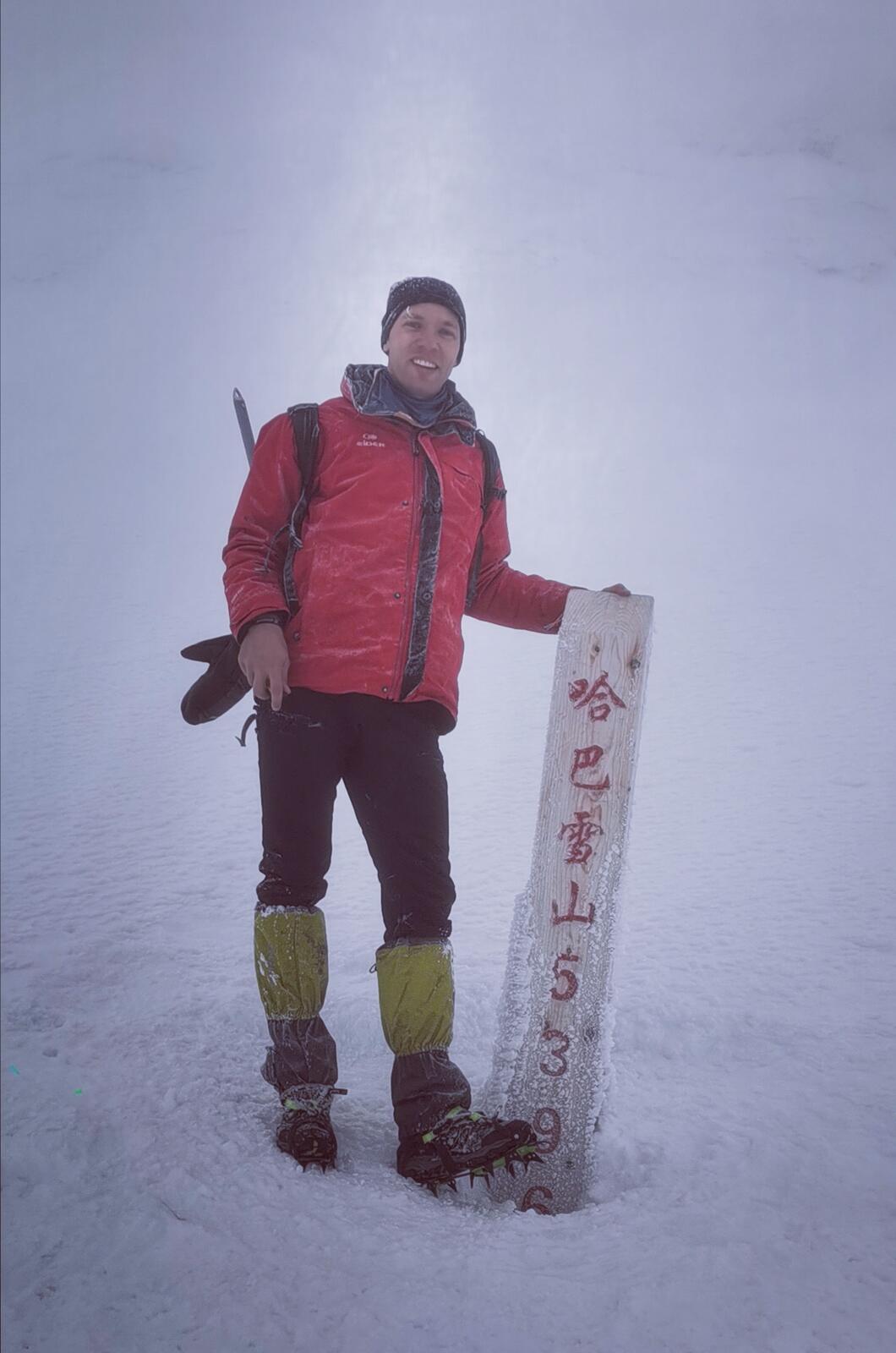 Two climbers at the Haba Snow Mountain summit sign in whiteout conditions.